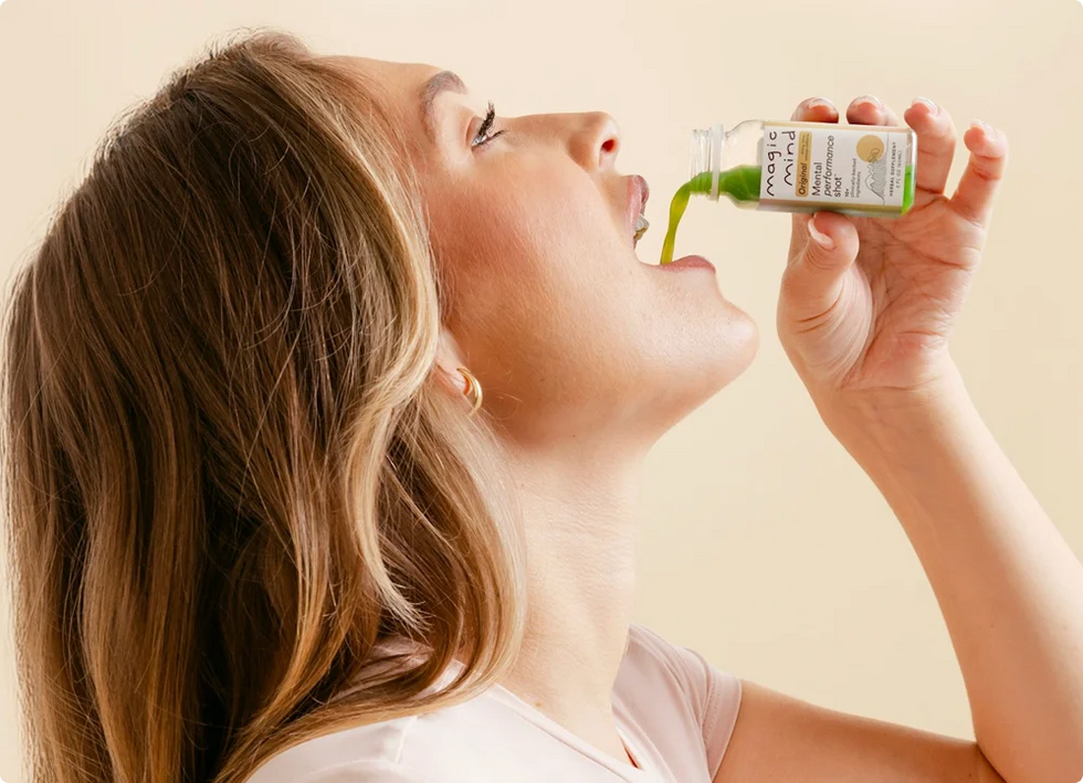Woman drinking a Magic Mind Mental Performance Shot against a beige background.
