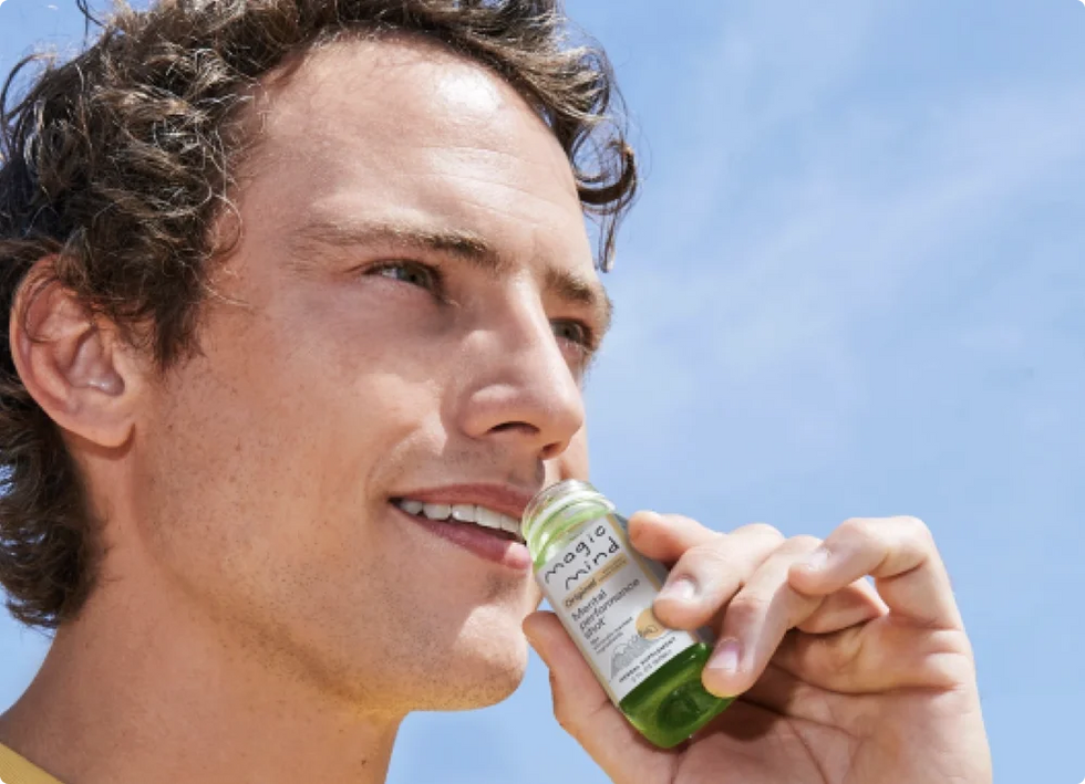 Man holding a Magic Mind Original Mental Performance Shot bottle outdoors.