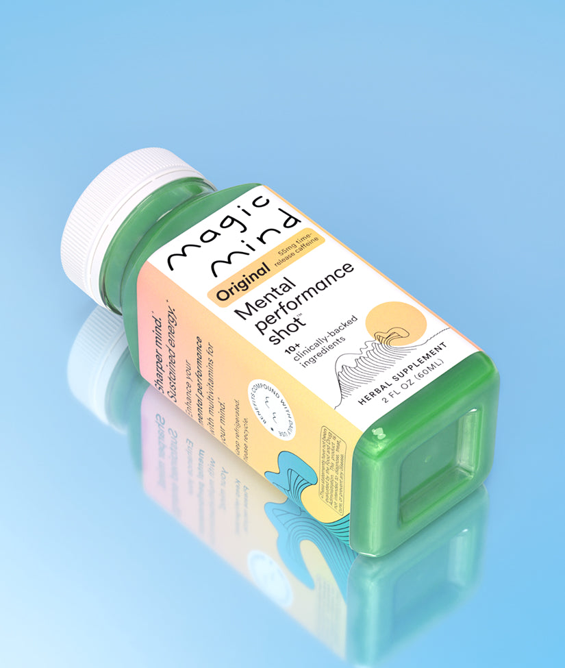 Magic Mind Original Mental Performance Shot bottle lying on its side against a light blue reflective background.