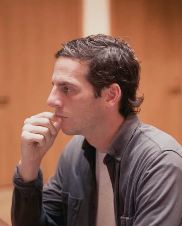 A profile shot of James Beshara, founder of Magic Mind, looking thoughtfully to the side with his hand resting near his chin, wearing a grey button-down shirt.