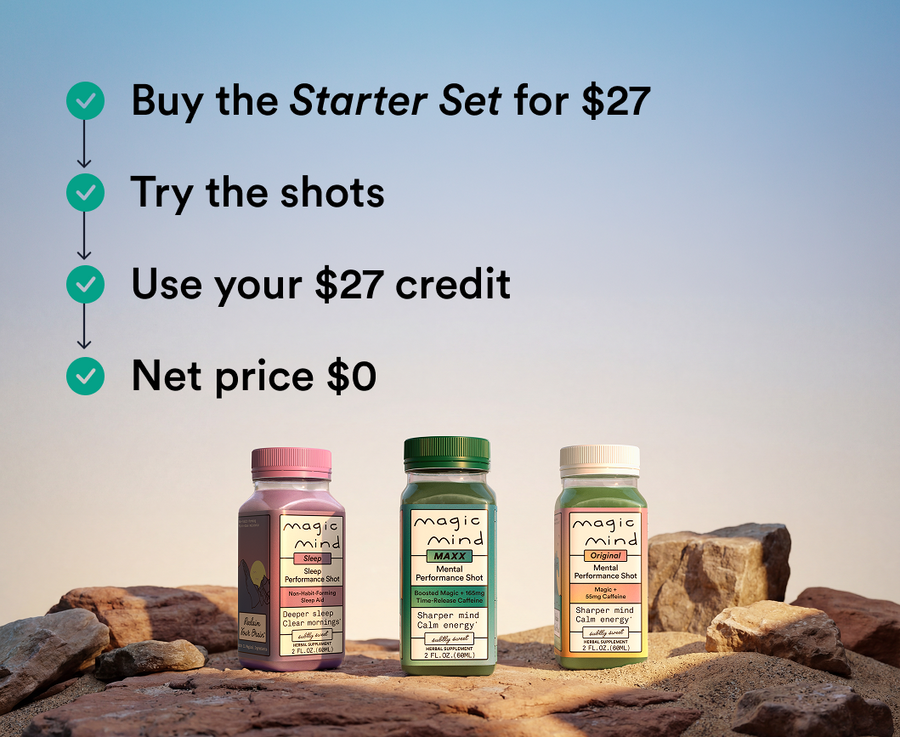 Three labeled bottles of Magic Mind mental performance shots in pink, green, and cream caps arranged on rocks against a blue 