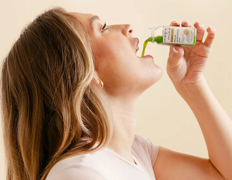 Woman drinking a Magic Mind Mental Performance Shot against a beige background.