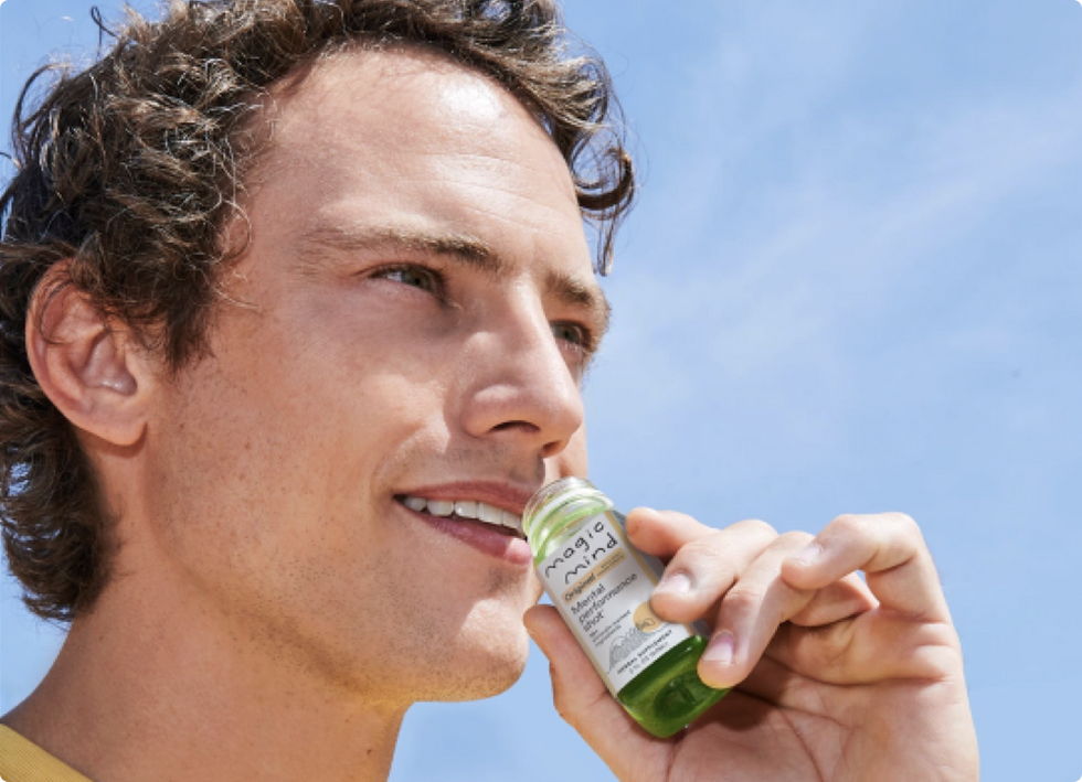 Man holding a Magic Mind Original Mental Performance Shot bottle outdoors.
